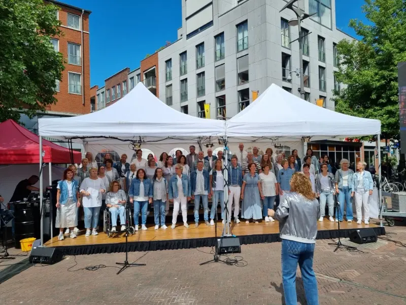 Foto van het volledige koor tijdens een optreden in de buitenlucht.